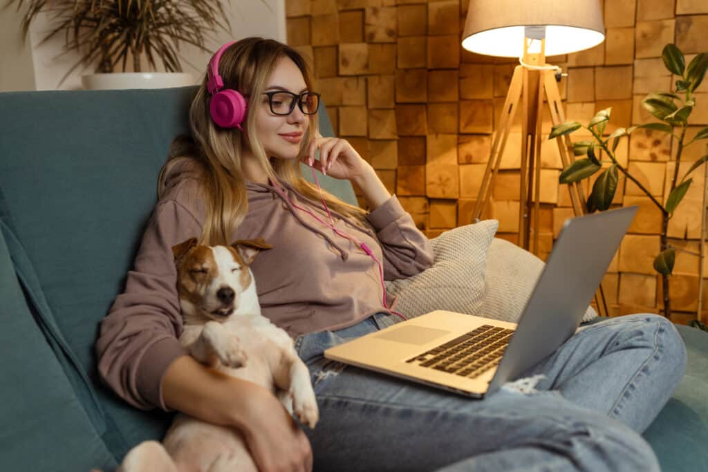 Woman on couch with dog watching Dreamforce online.